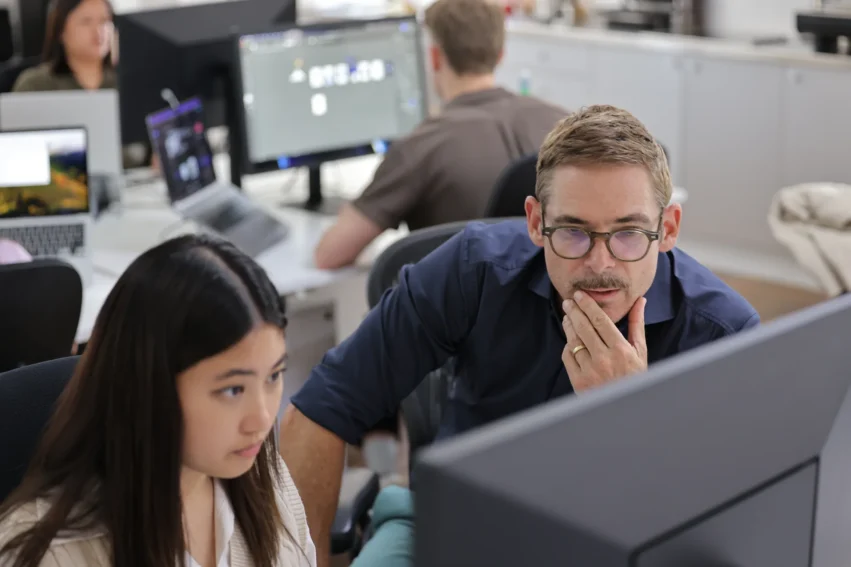 Two walterwakefield team members reviewing work on a monitor in a busy open-plan studio